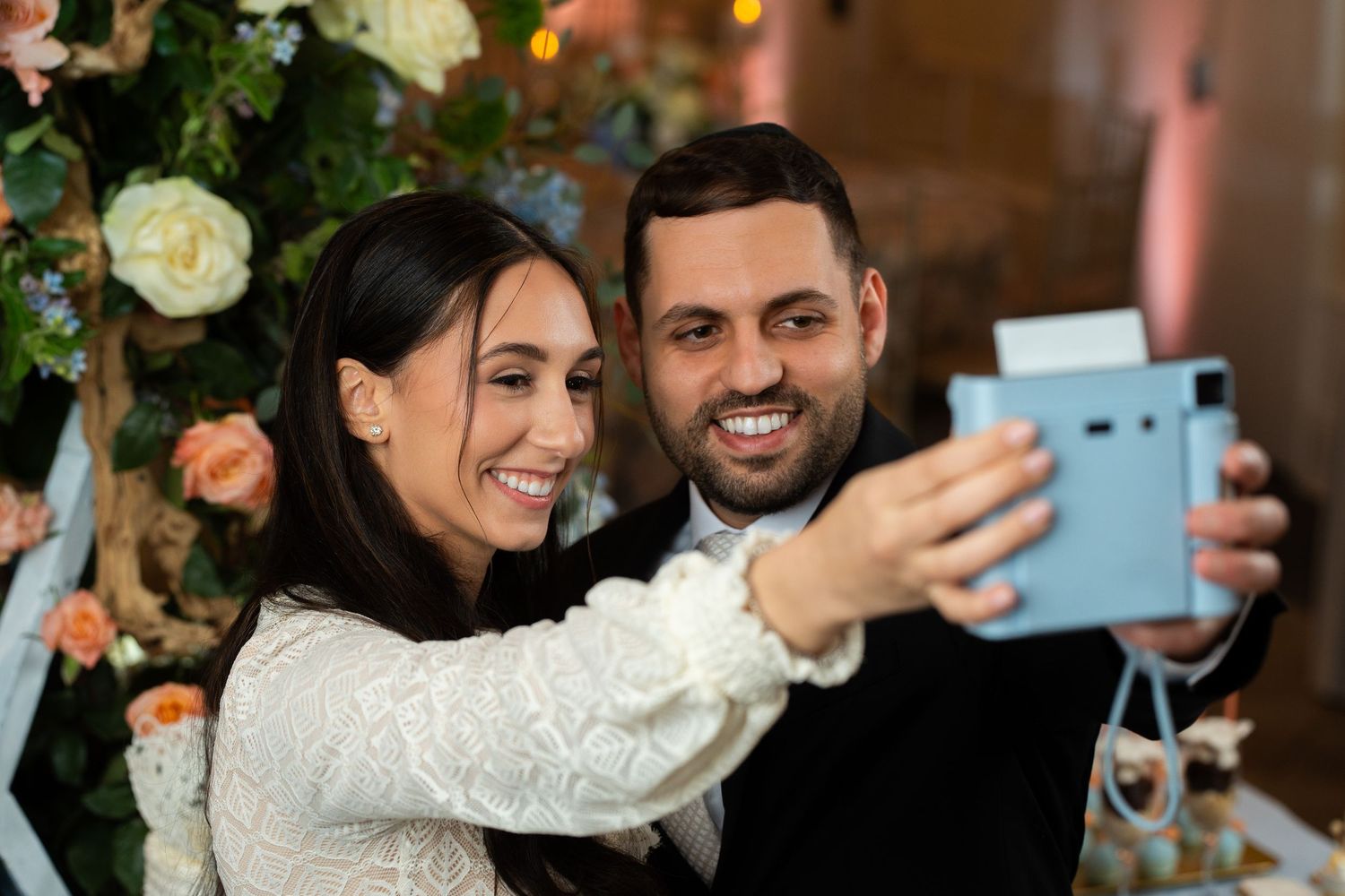 Wedding celebration selfies being taken at an indoor reception venue with floral decorations.
