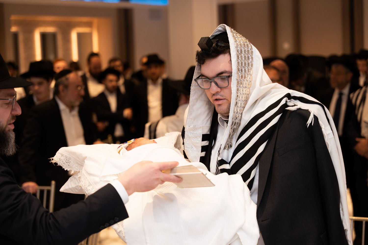 A group of people in traditional Jewish attire gather for a religious ceremony in an indoor setting.
