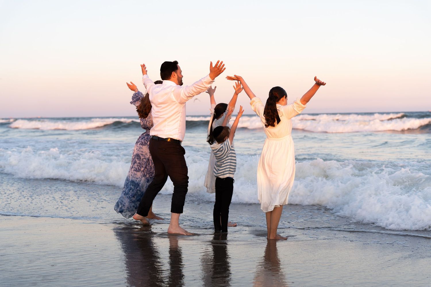 A group of people playing and splashing in the ocean waves during a sunset at the beach.