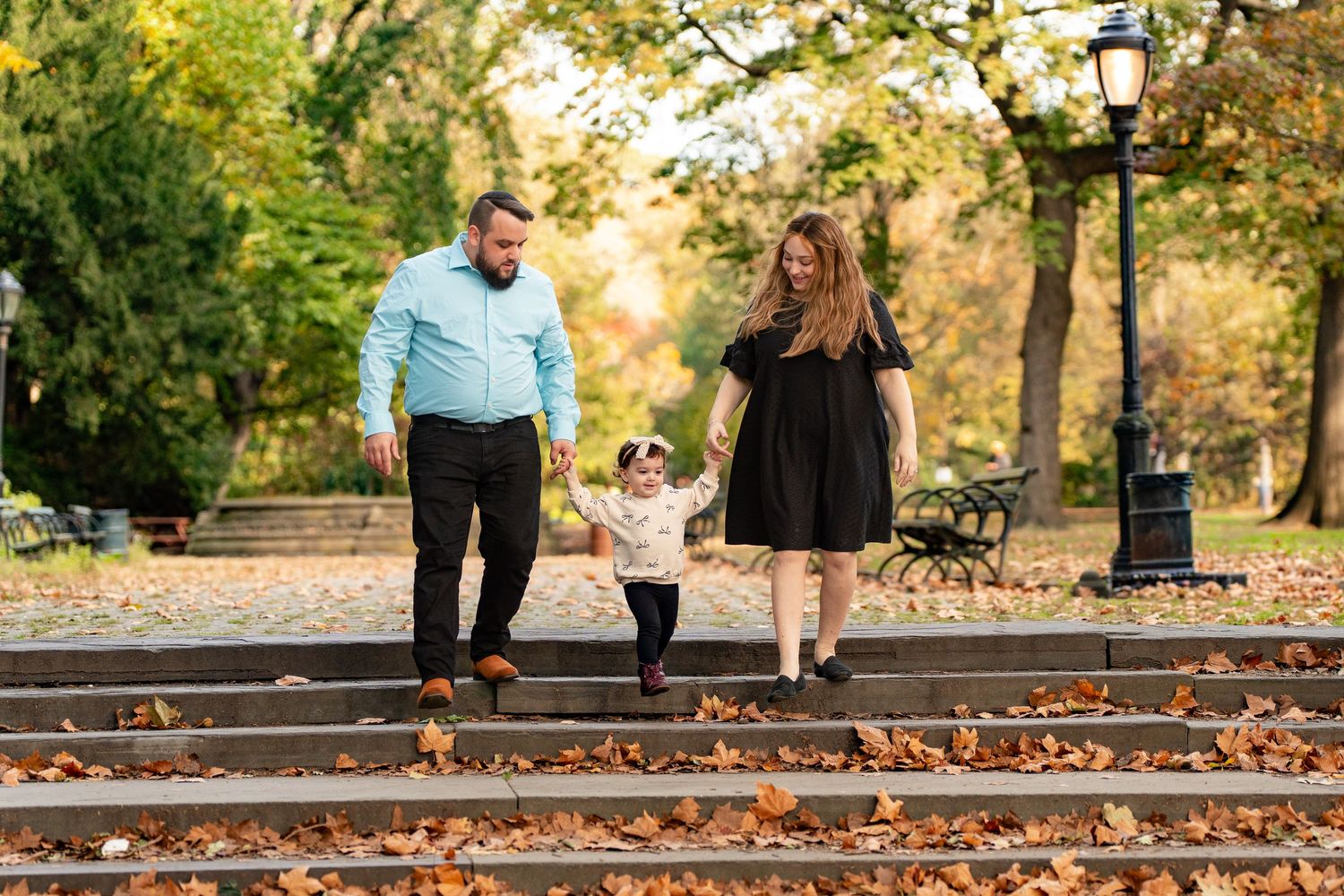 Family enjoying a walk together on autumn railroad tracks surrounded by fallen leaves at sunset.