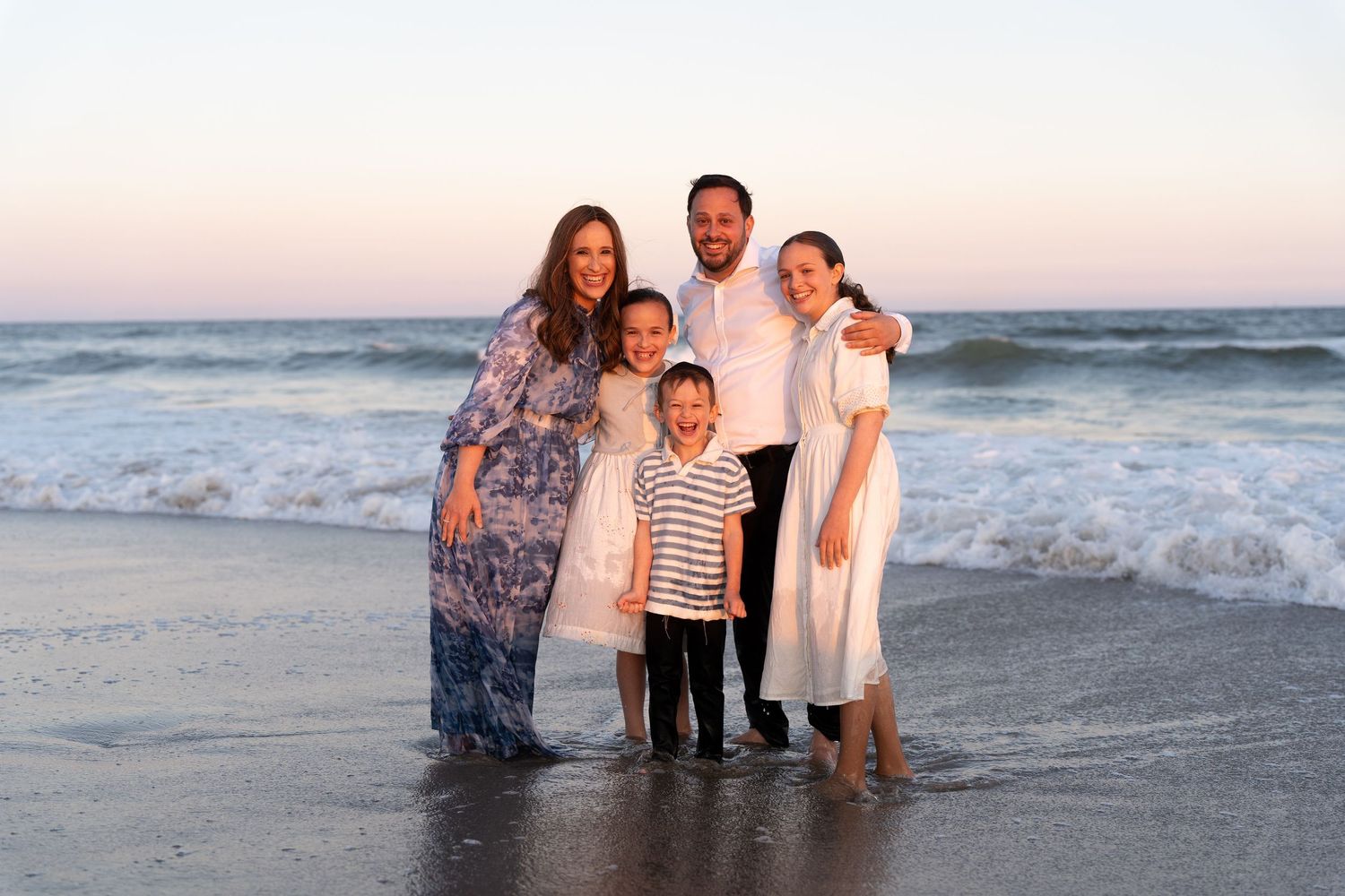 Family poses together at sunset on a beach with waves crashing behind them.