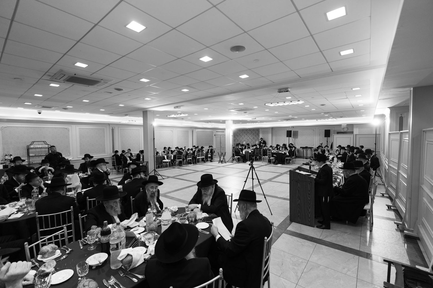 Black and white photo of a large Jewish banquet hall filled with guests dining at elegantly set tables.