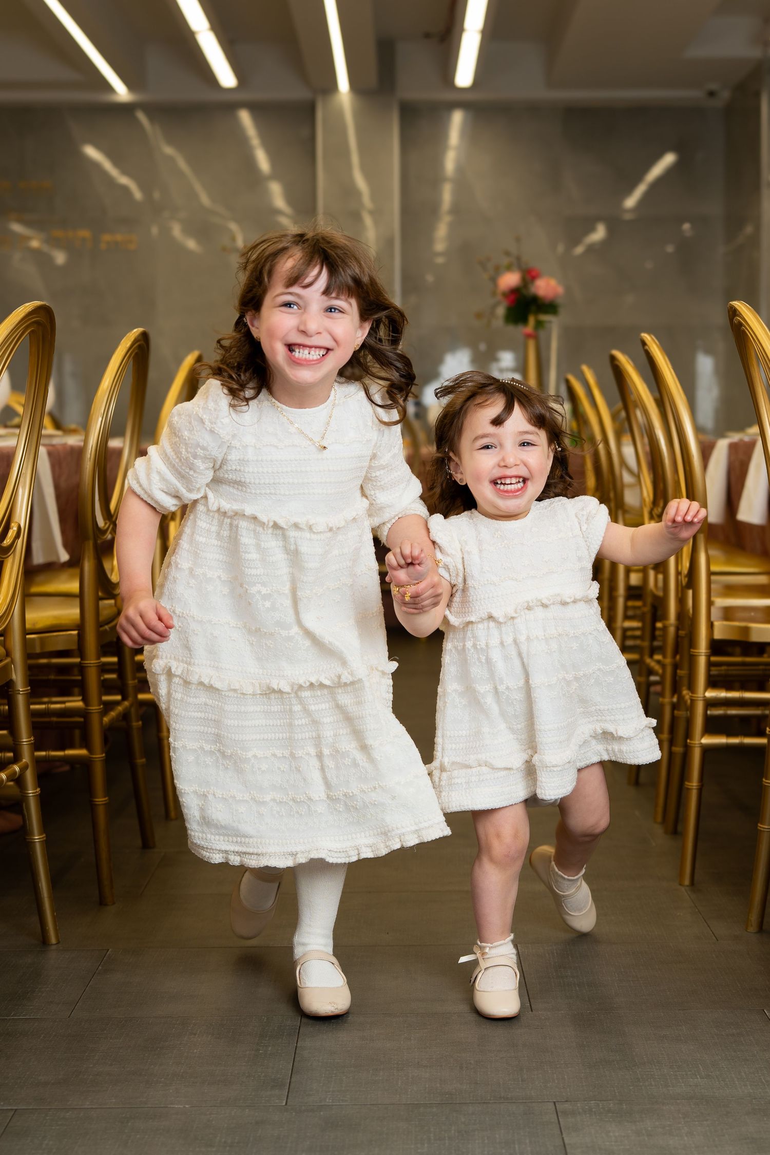 Flower girls in white dresses running and playing at a formal event.