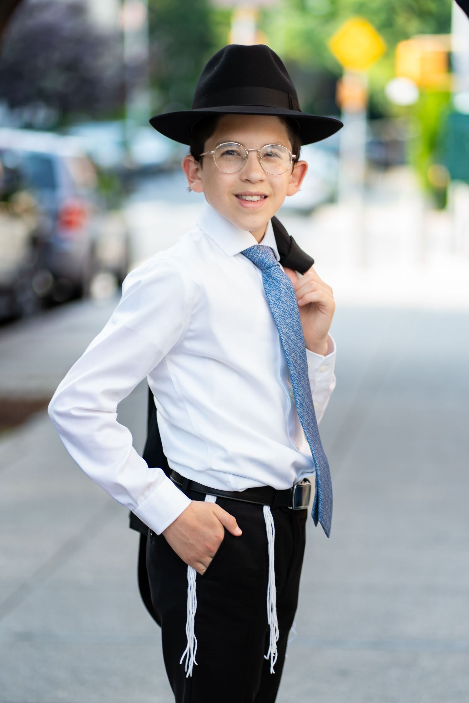 Young person in traditional Jewish attire with white shirt and black hat outdoors.