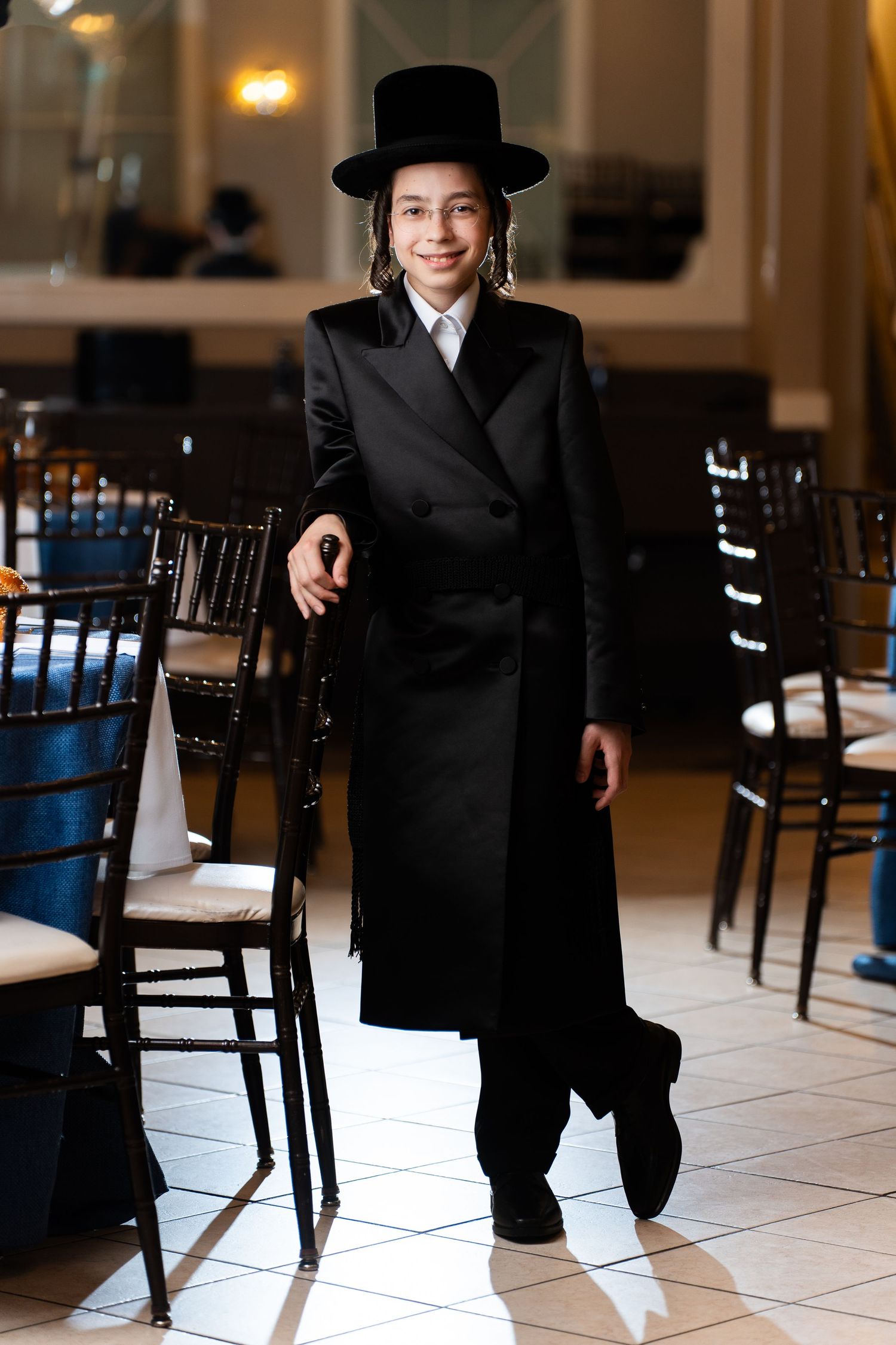 Sequence of formal poses in traditional black attire against tiled floor and chairs.