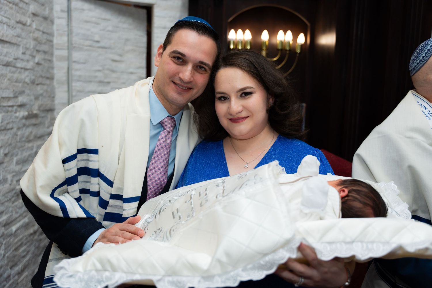 A Jewish baby naming ceremony with parents holding their newborn wrapped in white lace during the traditional celebration.