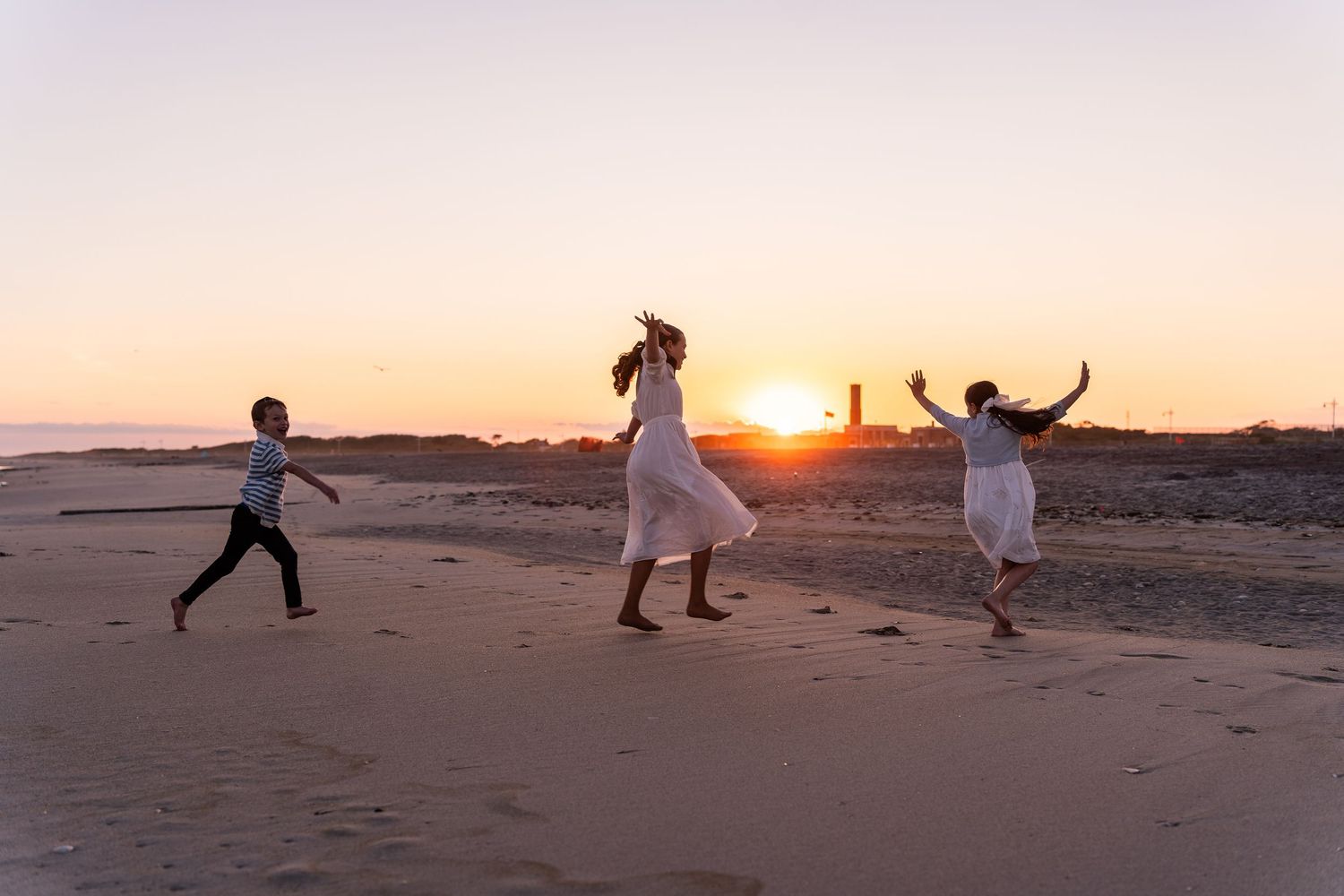 Silhouettes of people dancing and jumping on a beach at sunset with golden light illuminating the scene.