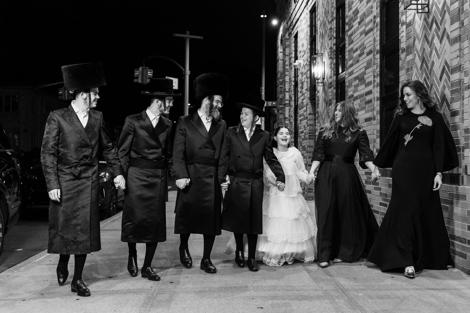 Black and white photo series showing a wedding party walking and posing along a stone wall exterior.