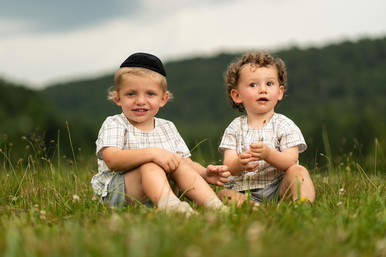 Children sitting together in a grassy meadow on a sunny summer day with hills in the background.