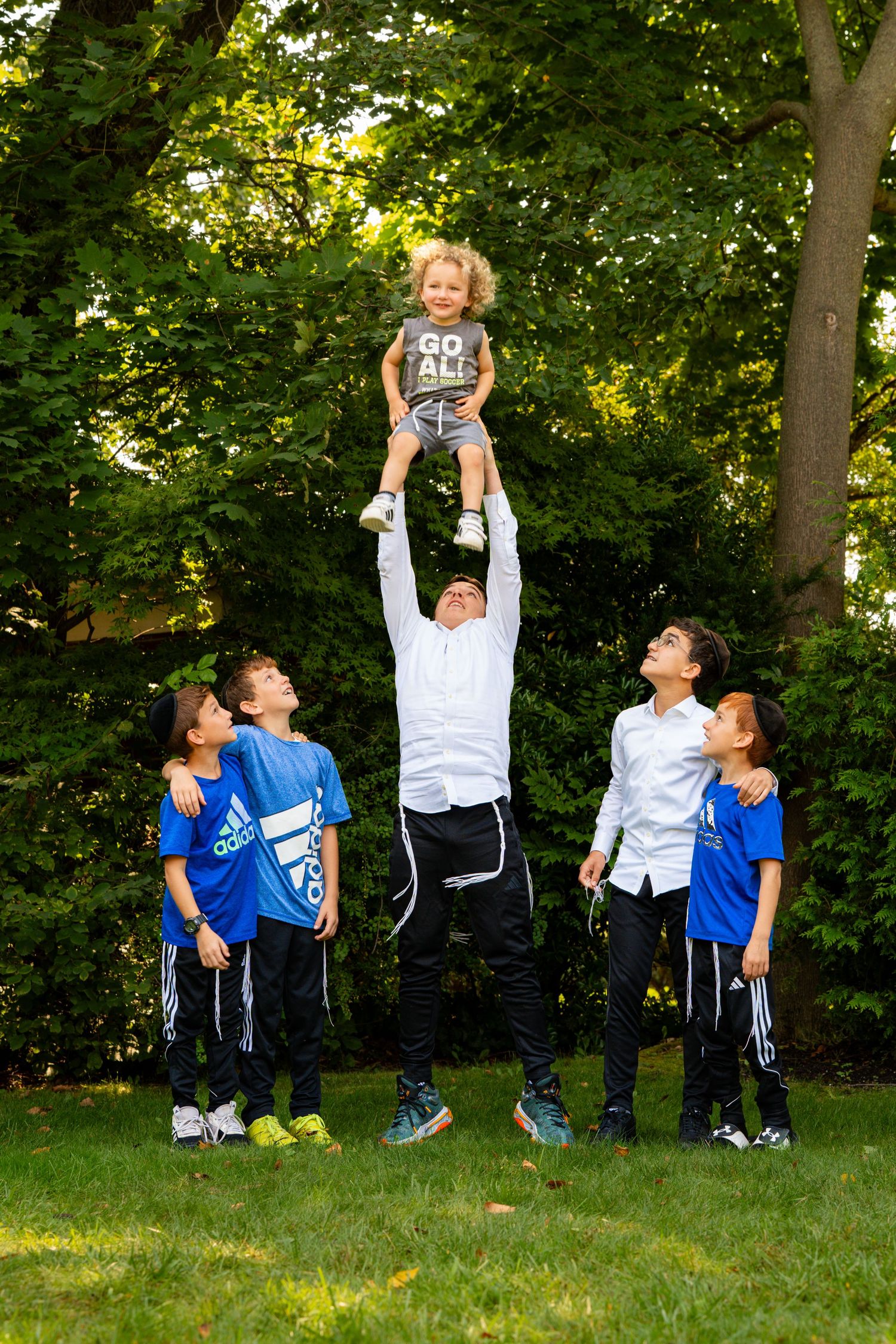 A sequence of children playing and jumping together on grass in a park setting.