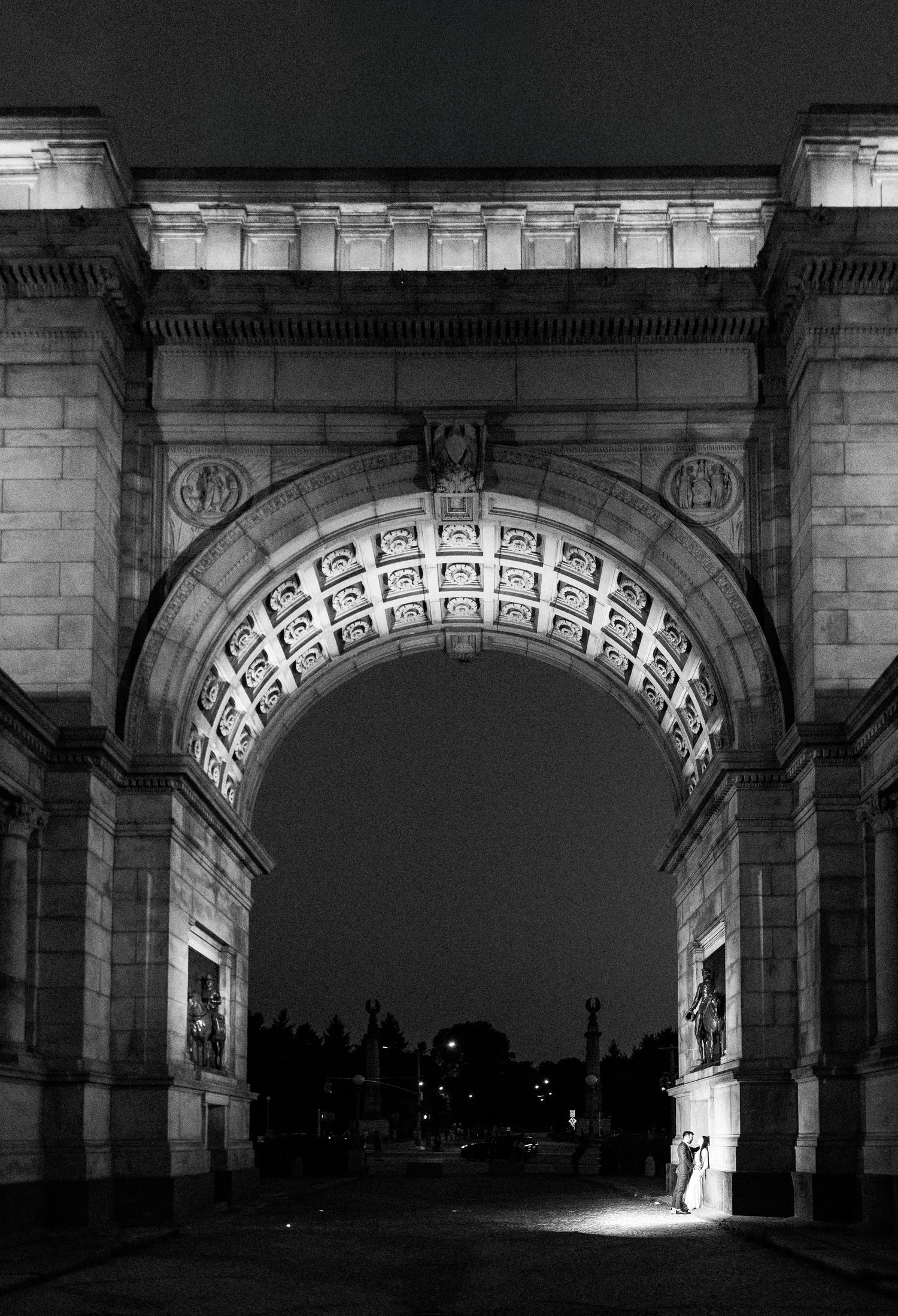 Black and white night photo of the grand illuminated arch at Grand Army Plaza, Brooklyn, NYC.