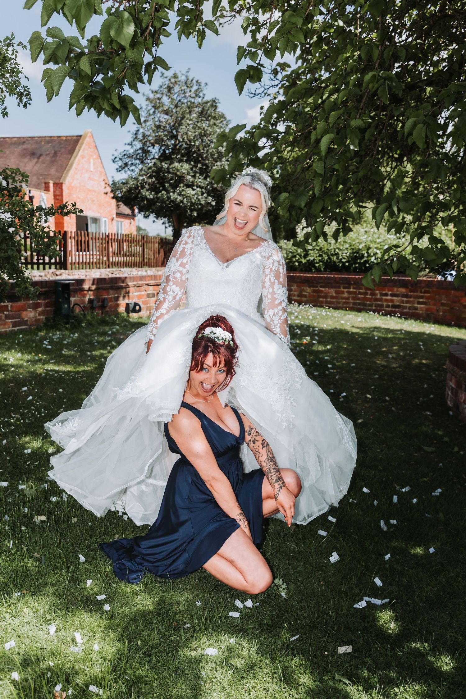 Two people share a tender moment outdoors in a garden setting with flowing white fabric and navy blue attire.