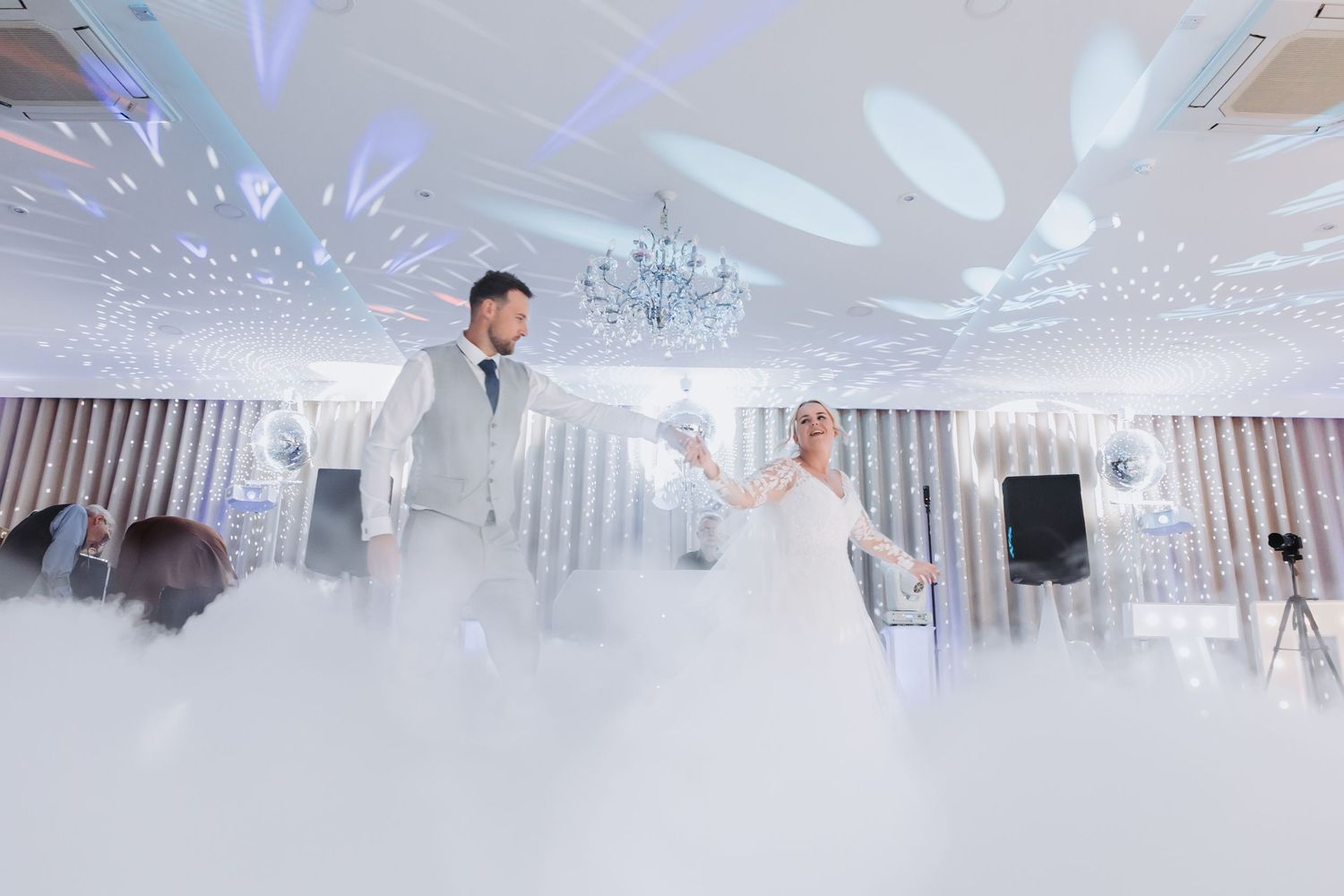 A modern white event space with crystal chandeliers and LED lighting creating an elegant atmosphere.