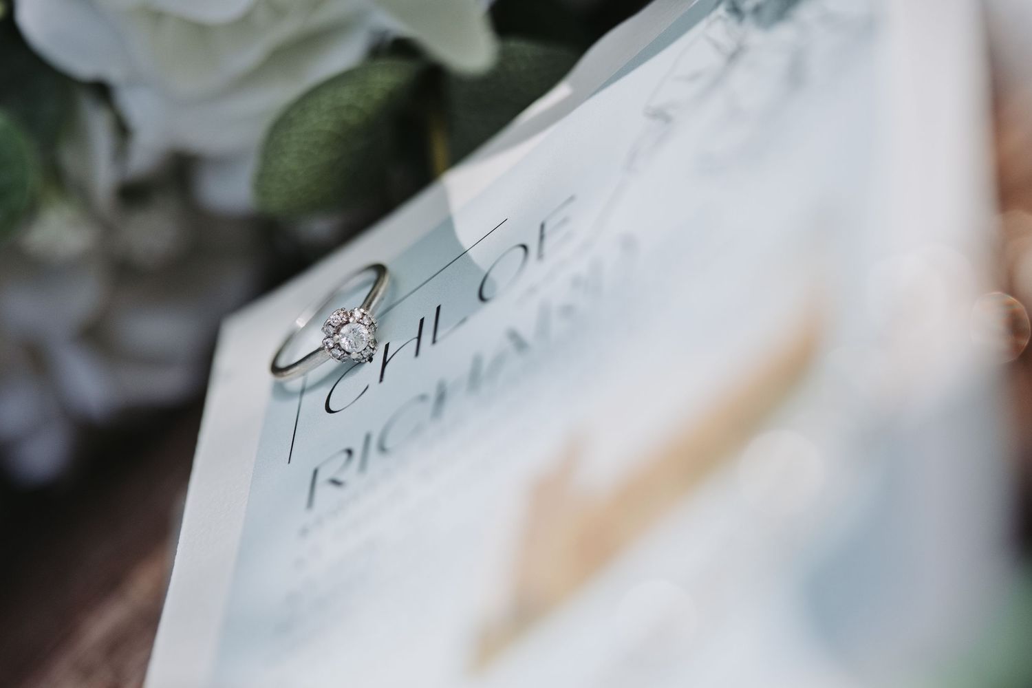 Close-up of elegant wedding rings resting on a wedding invitation with floral decor in the background.