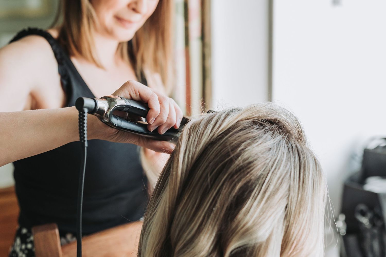 Hairstylist using professional tools and equipment to style client's blonde hair in a modern salon setting.