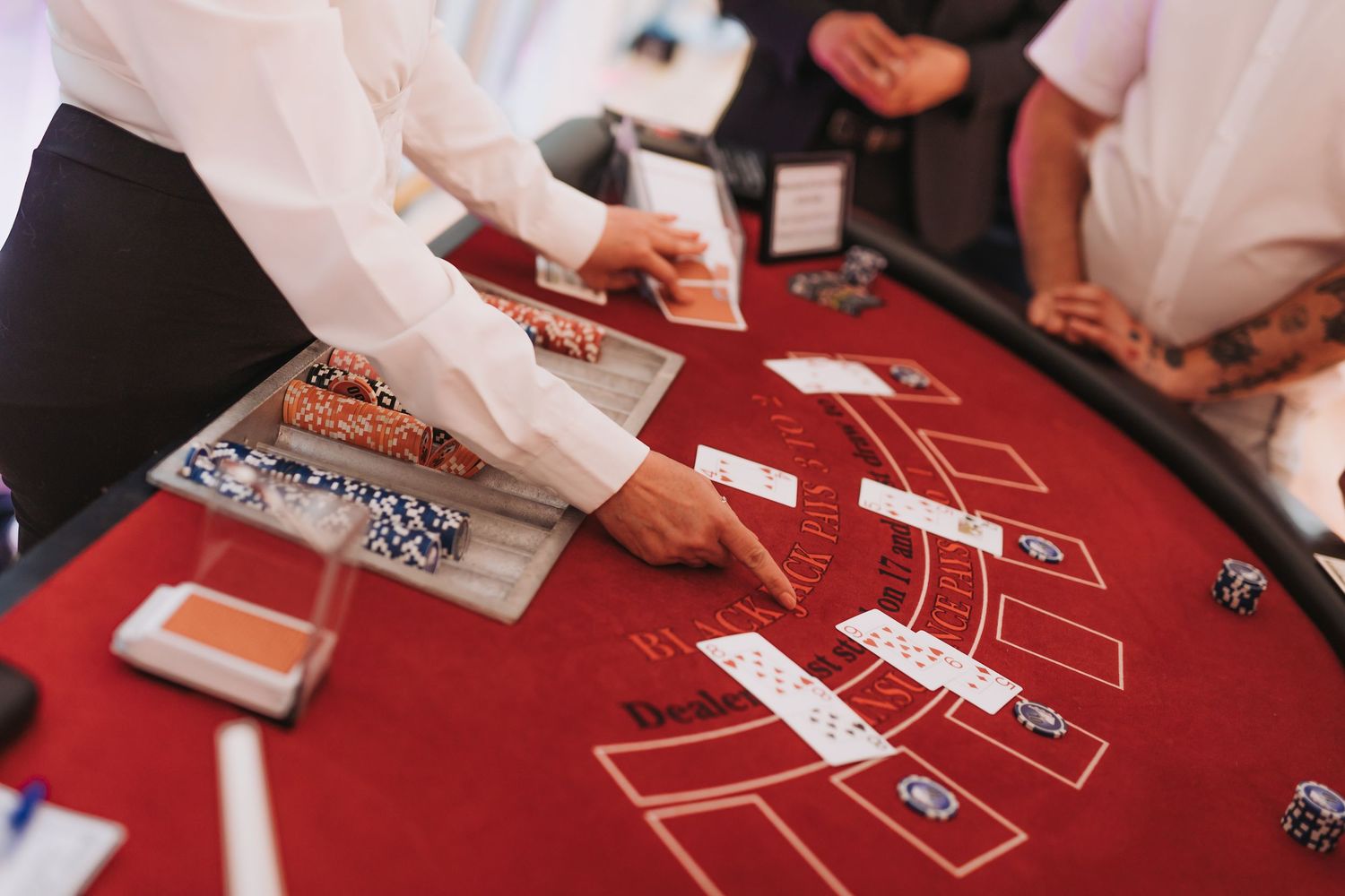 Overhead view of a red casino blackjack table with players' hands and cards visible during gameplay.