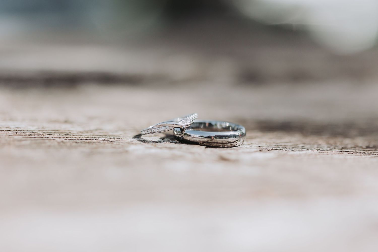 Two silver wedding bands with diamond accents resting on a rustic wooden surface with soft bokeh background.