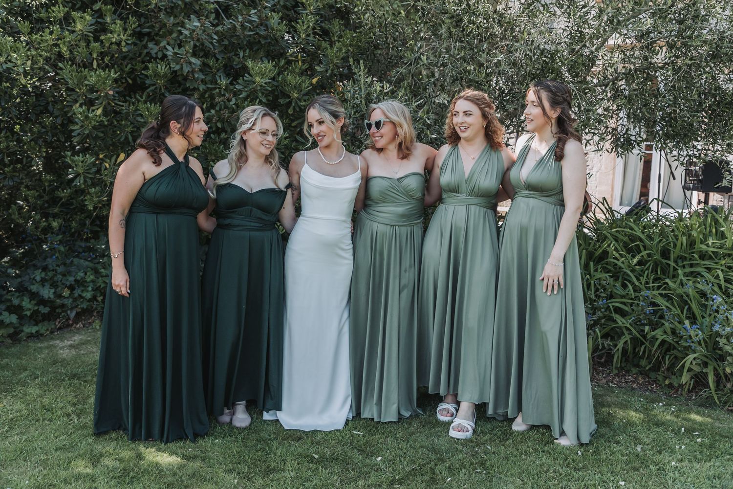Wedding party wearing sage green and white dresses posing together in an outdoor garden setting.