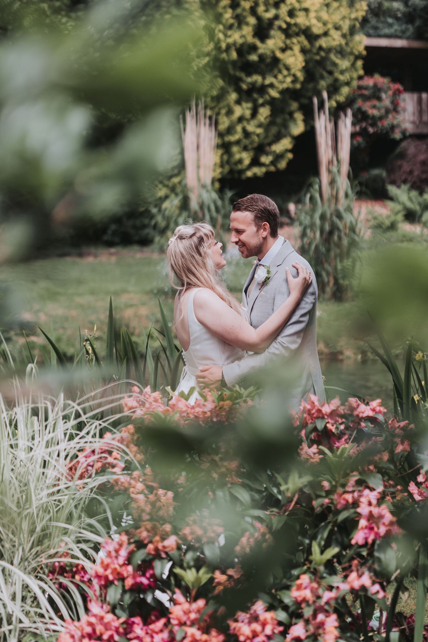 A bride and groom share a romantic moment surrounded by lush gardens and pink flowers on their wedding day.