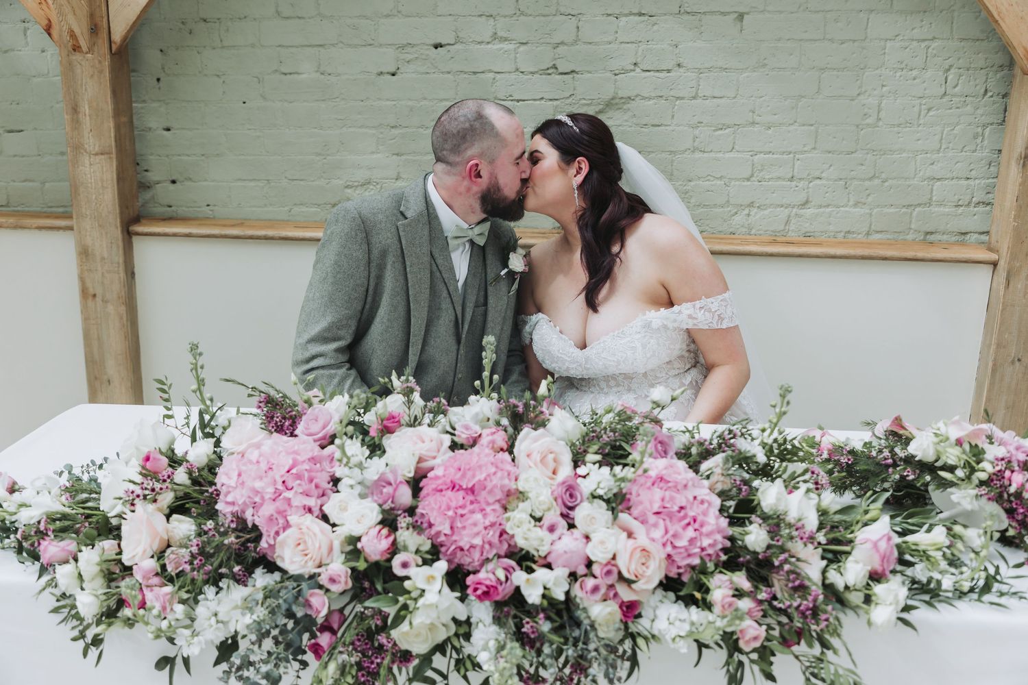 Wedding venue decorated with lush pink and white floral arrangements against a white brick wall backdrop.