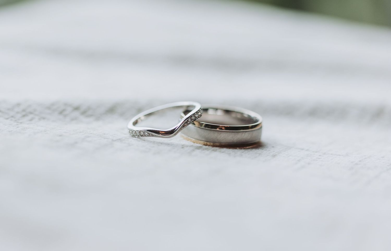 Two silver wedding bands, one with a curved diamond design, resting on an open book in soft focus light.