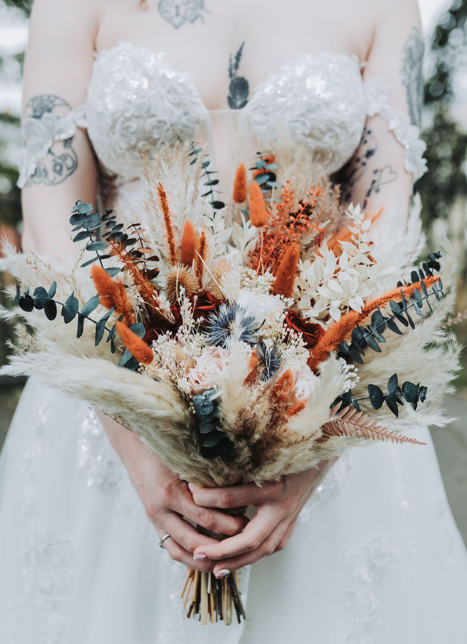 A rustic dried flower wedding bouquet featuring white pampas grass, eucalyptus, and burnt orange accents.