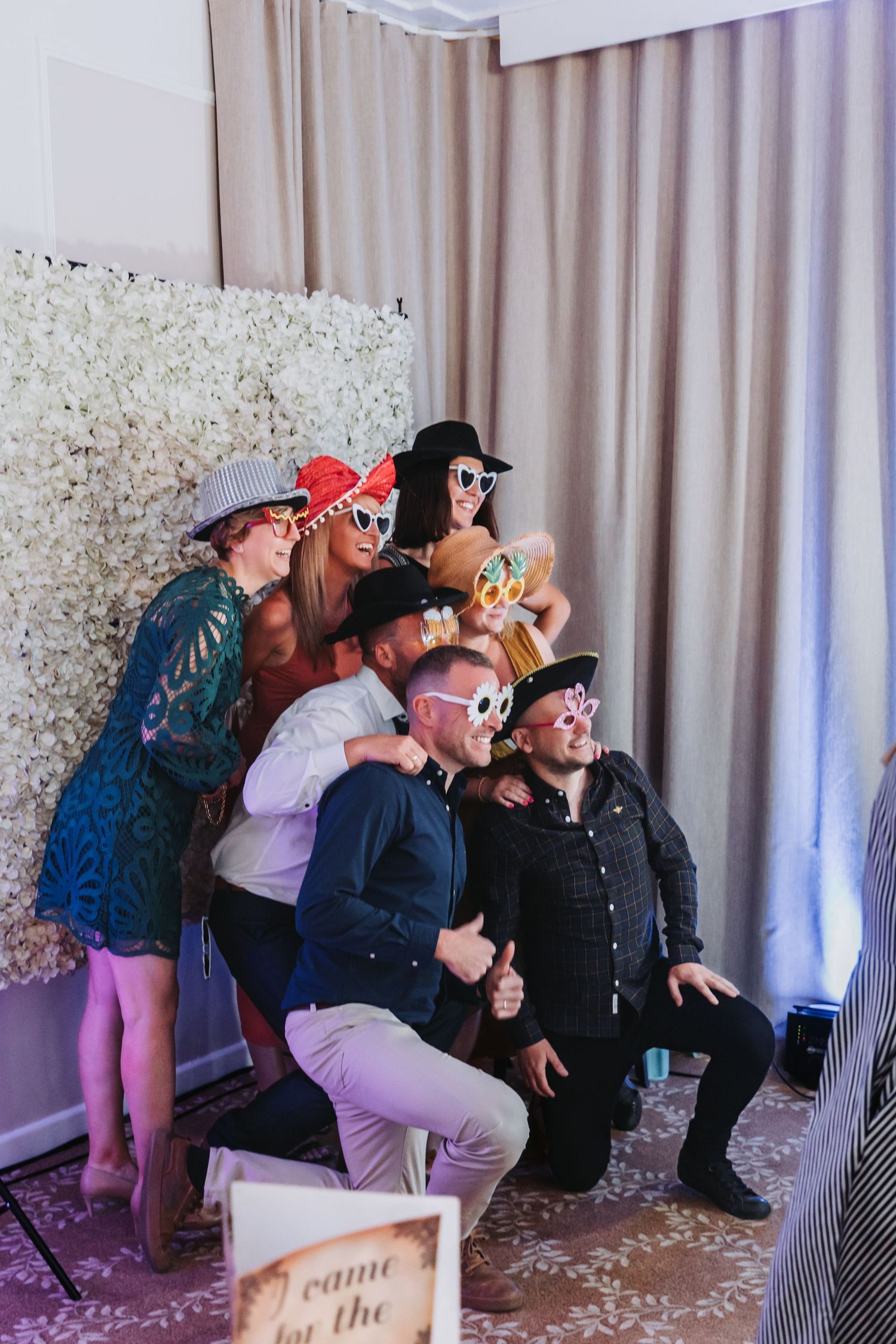 Group of wedding guests sitting together wearing black hats and taking shots during a celebration.