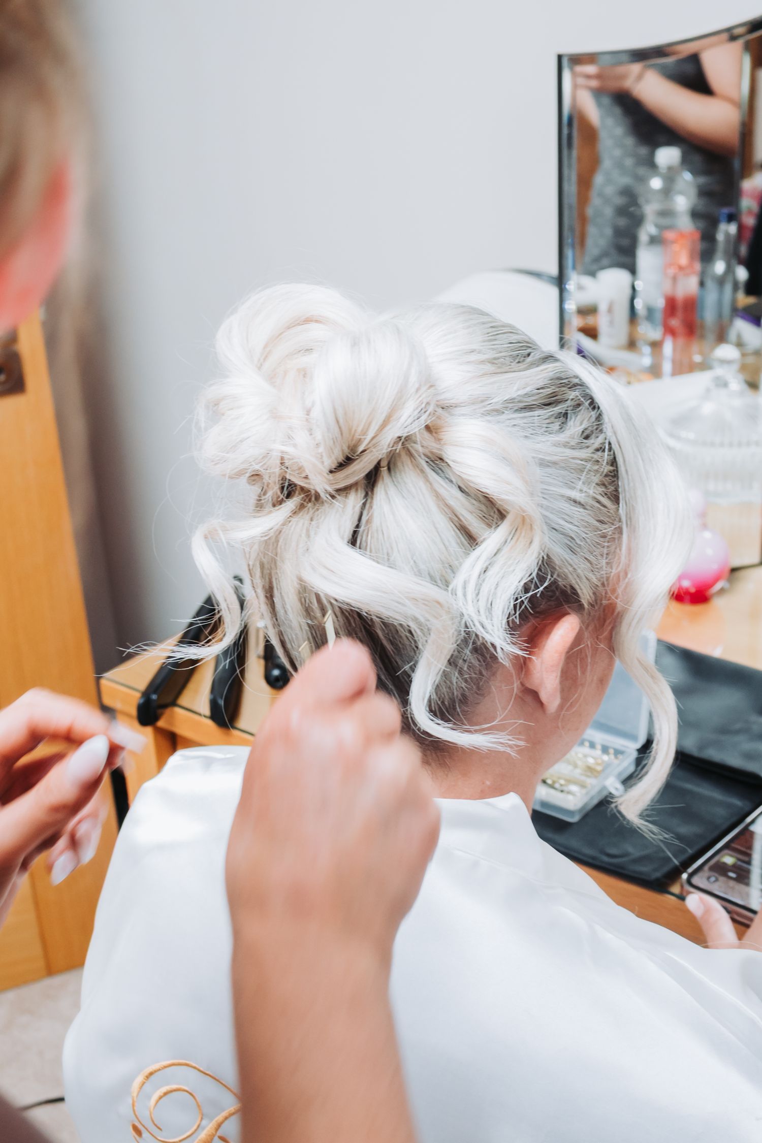 Hairstylist styling platinum blonde hair in an elegant updo at a beauty salon.