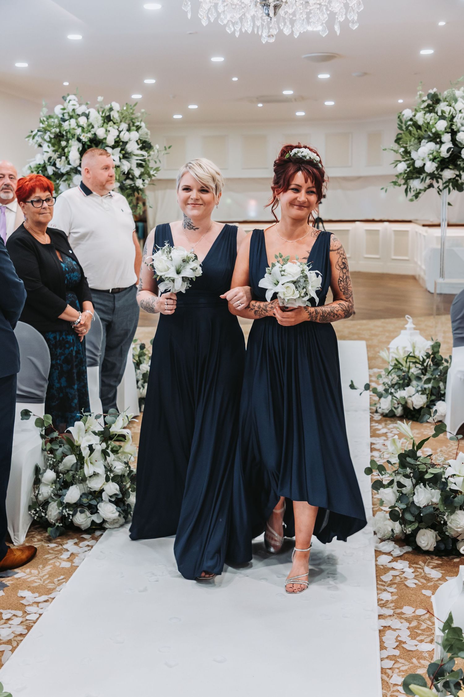 Navy blue bridesmaid dresses complement white floral arrangements in an elegant wedding ceremony setting.