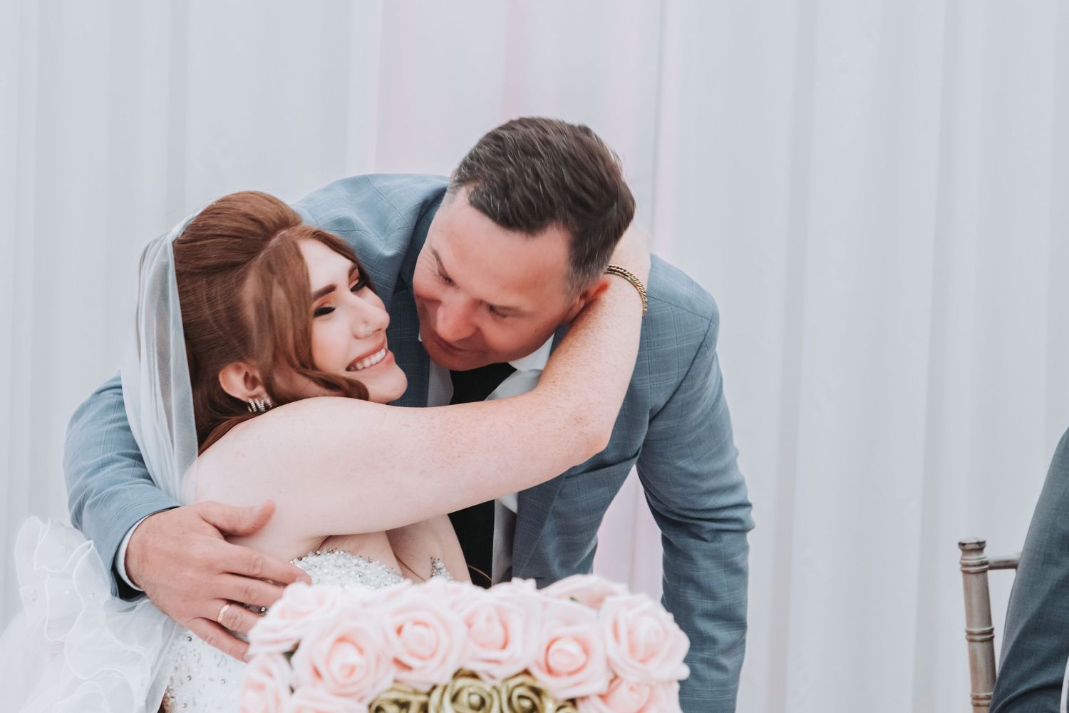 Romantic wedding couple embracing with soft pink roses in the background.