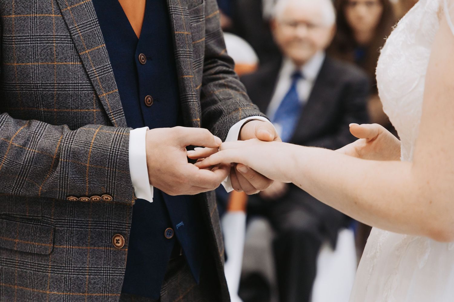 Close-up of wedding ring exchange during ceremony with plaid suit detail.