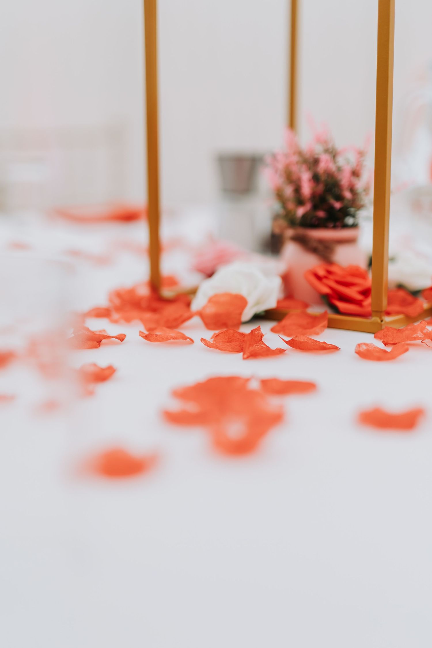 Gold candle holders stand among scattered coral-colored paper decorations on a white surface.