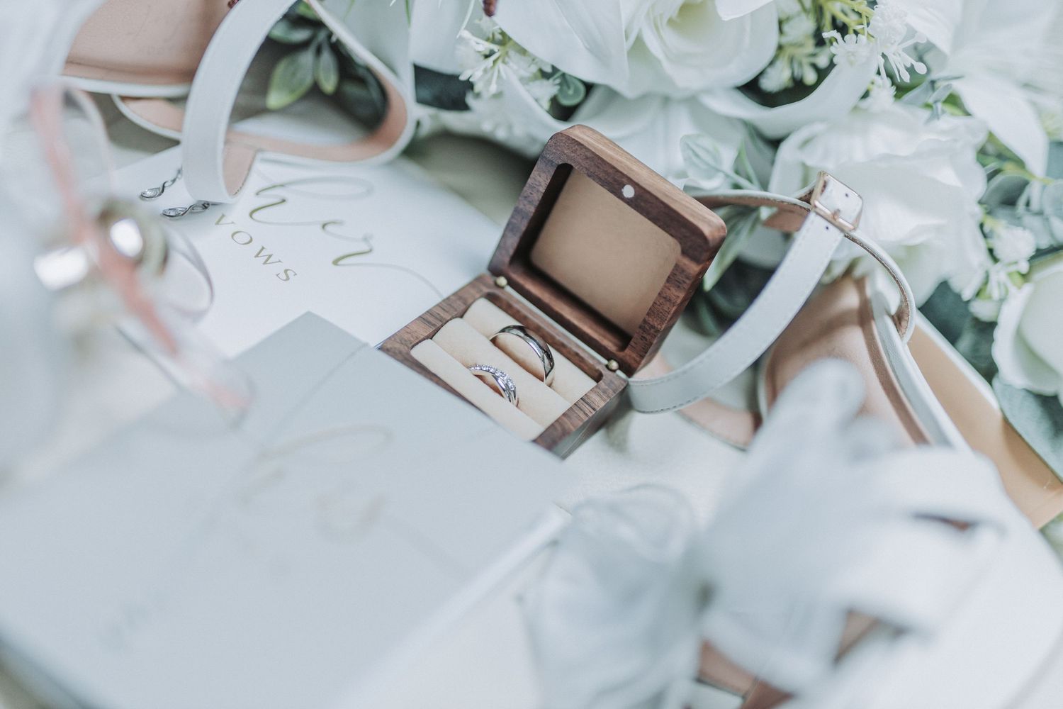 Flatlay of white flowers, makeup brushes, and cosmetic products arranged on light marble surface.