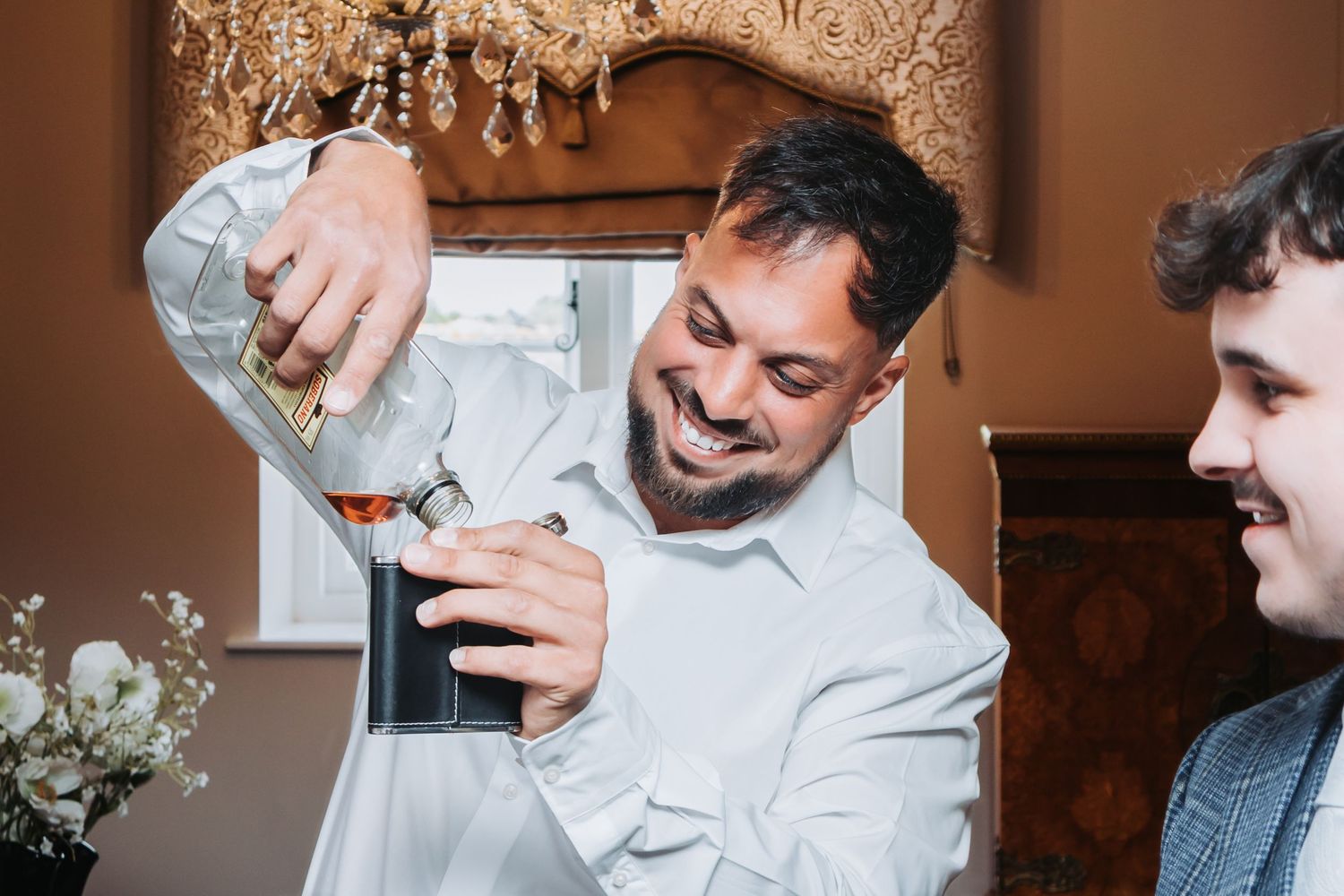 Chef in white uniform pours liquid into a glass while preparing cocktails at a bar counter.