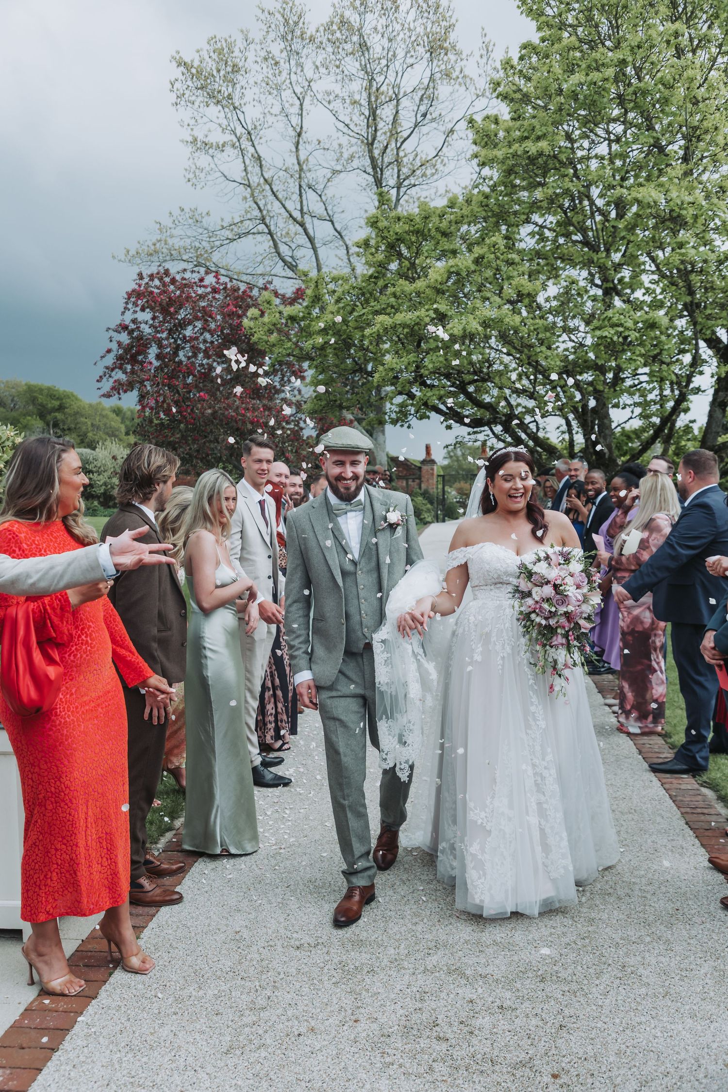 Wedding guests line up to congratulate the newlyweds during an outdoor celebration on a gravel path.