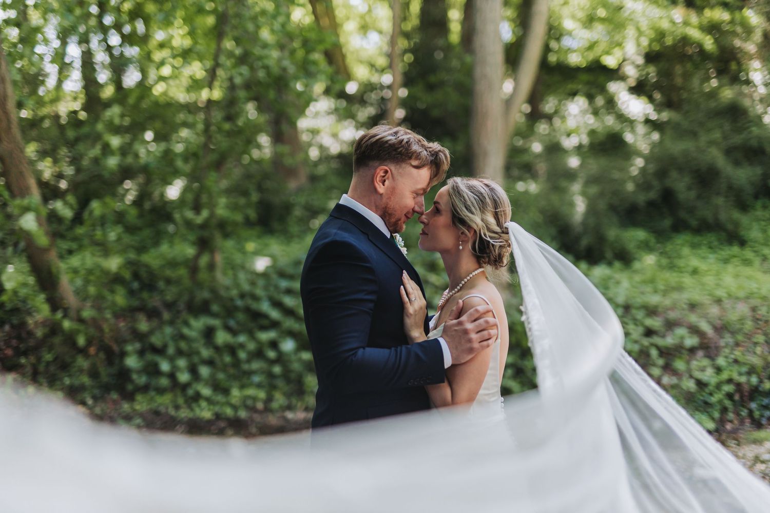 A romantic wedding portrait shows a couple embracing in a lush garden setting with flowing veil.