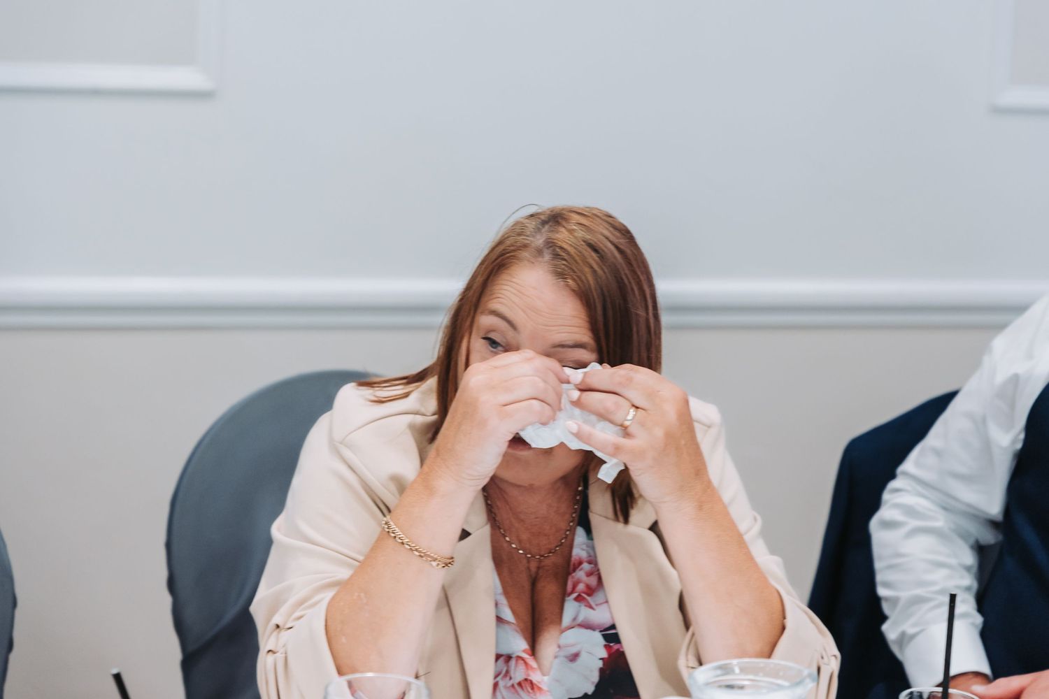 A person at a desk wipes their face with a tissue while showing signs of distress during a work meeting.