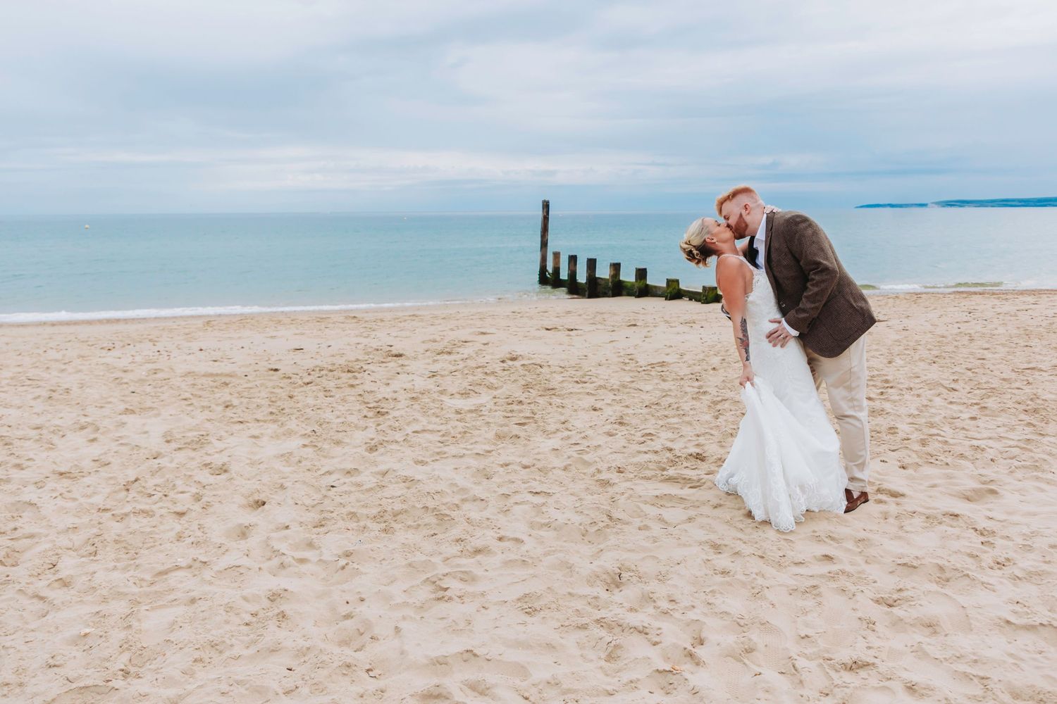 A romantic beach wedding moment with waves and wooden posts in the background.