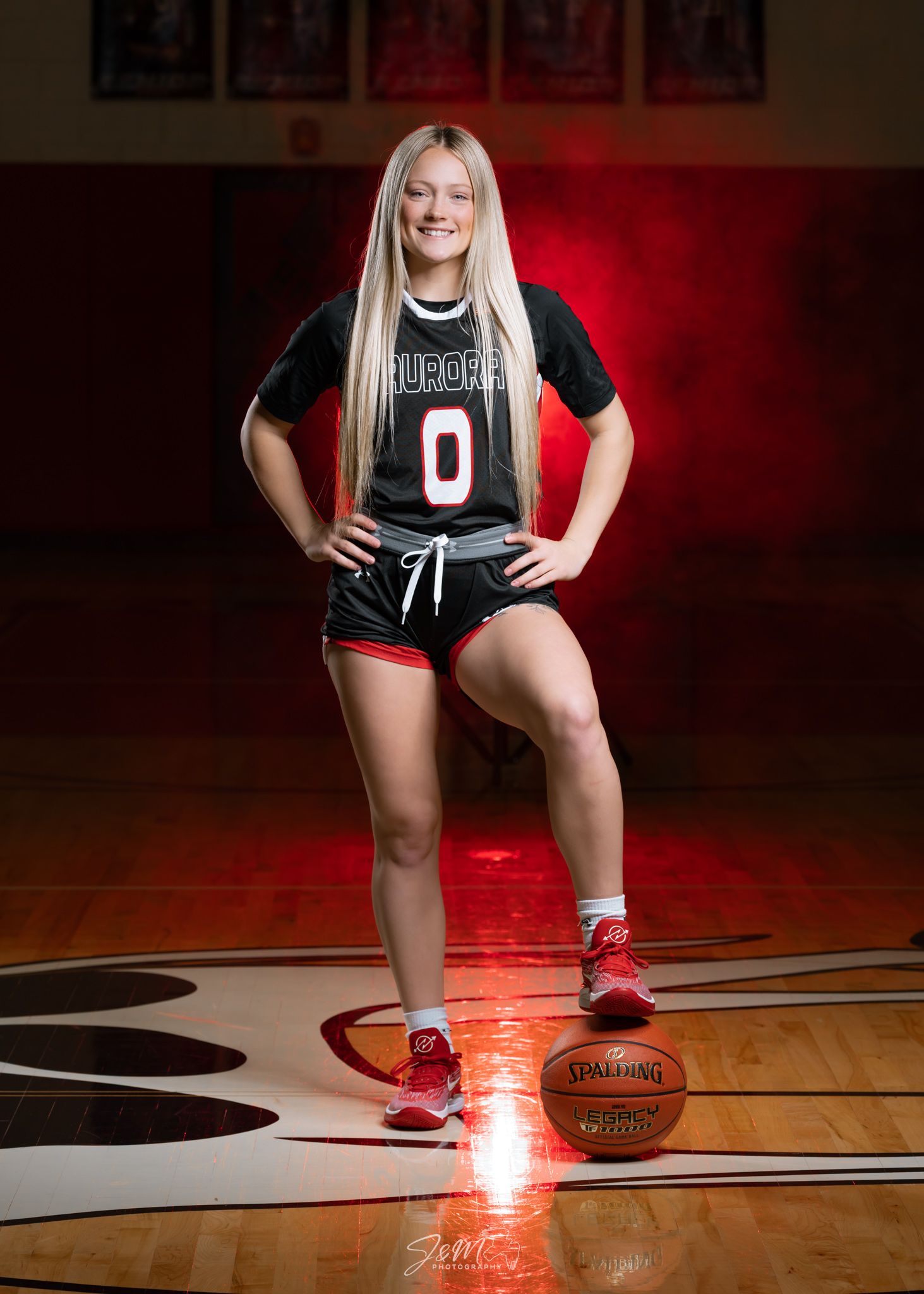 Basketball player poses with ball on court wearing black uniform number 0.