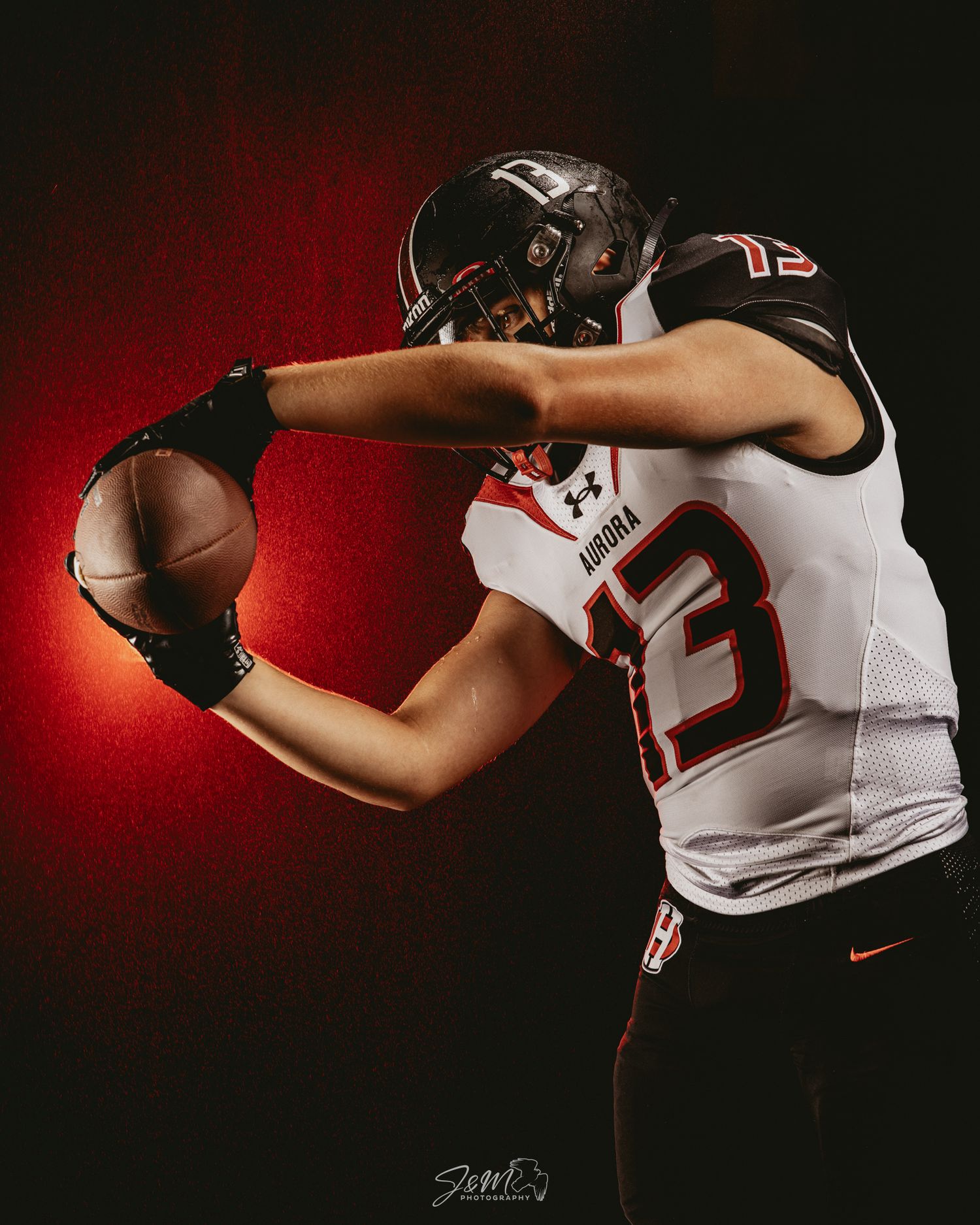 Football player in white jersey catches ball against dramatic red background.