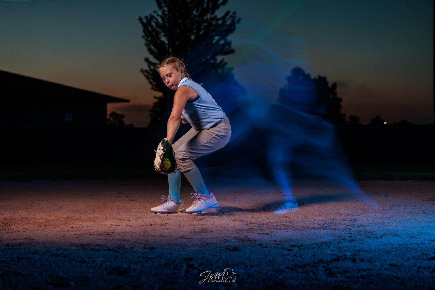 Baseball player poses at dusk with motion blur effect in blue light.