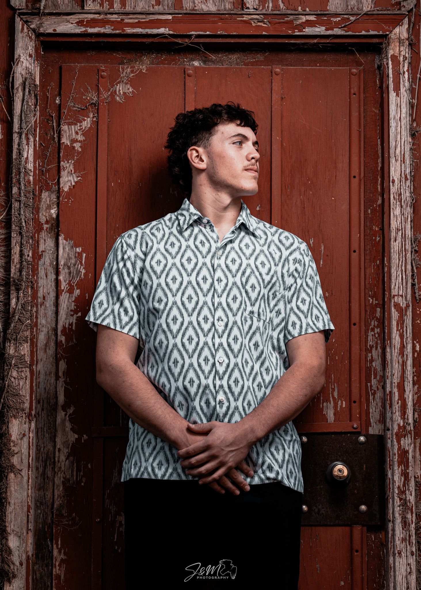 Portrait against a weathered red door showing a pattern shirt and dramatic lighting.