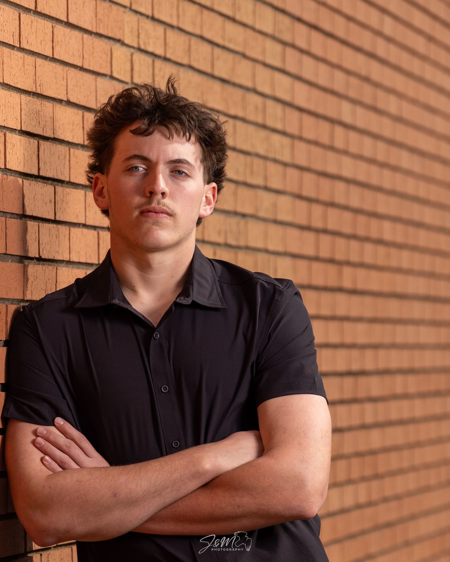 Portrait of person in black polo shirt against brick wall background.