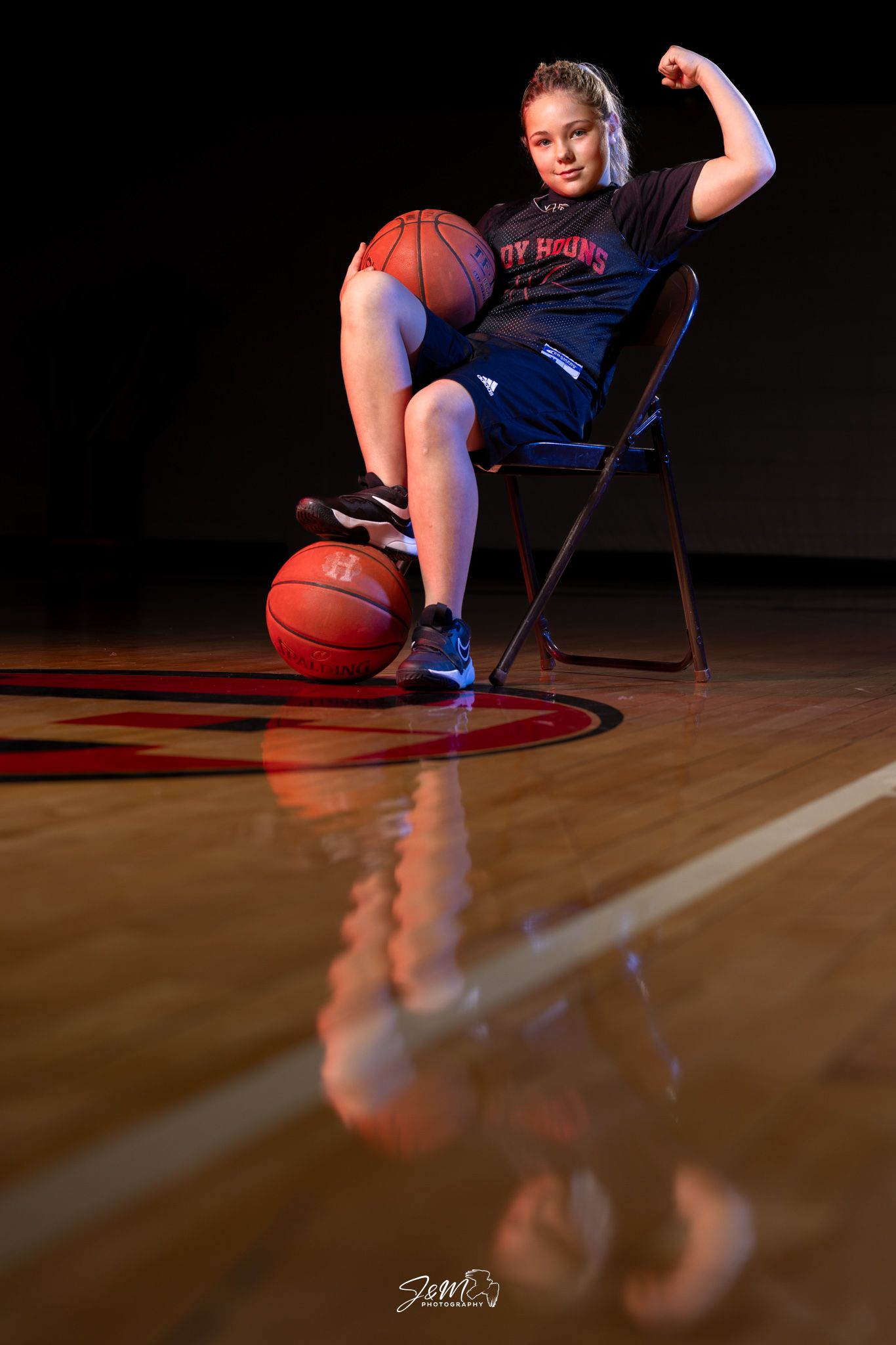 Athlete poses with basketball in dramatic lighting on court with reflection.