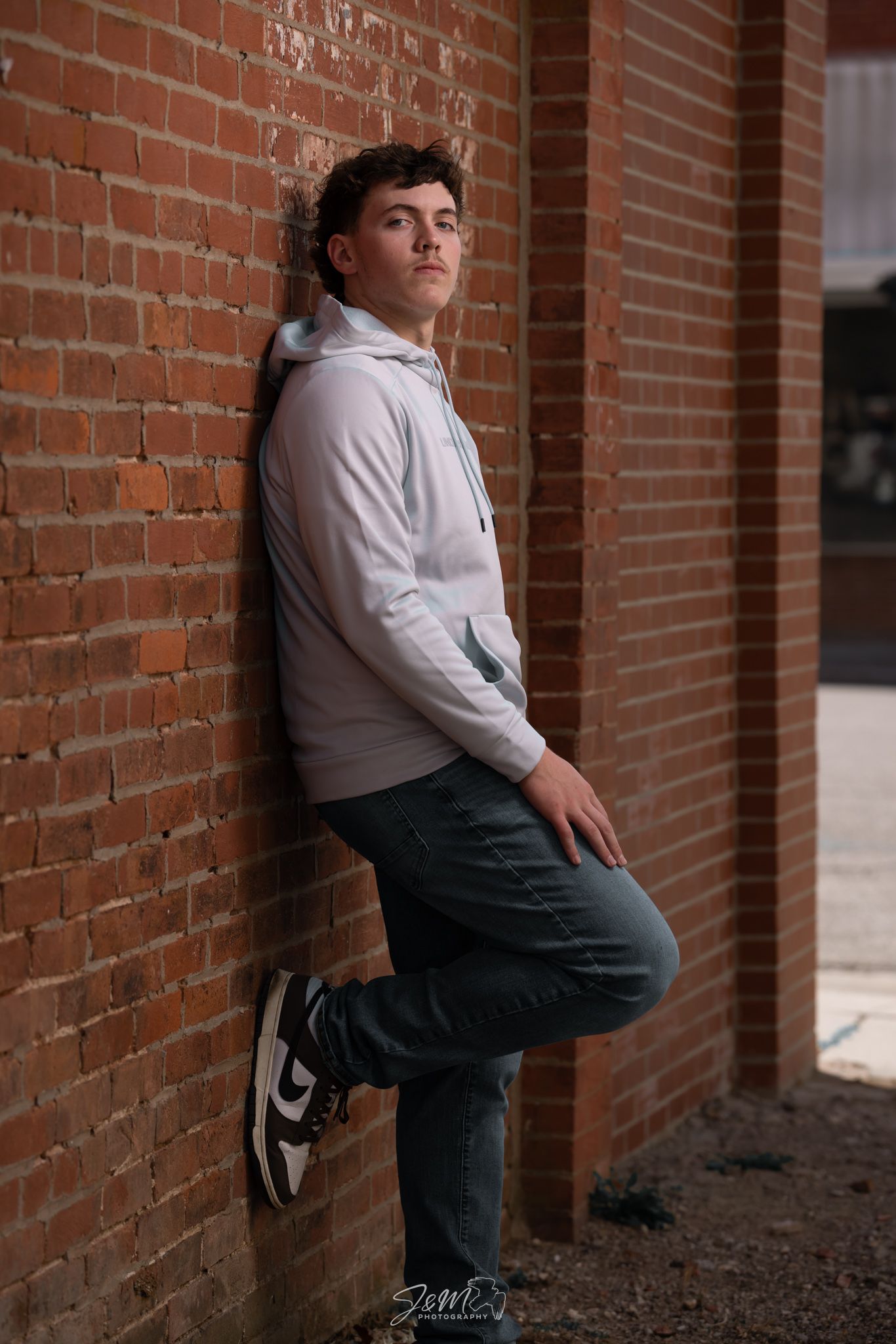 Casual portrait against brick wall wearing light hoodie and jeans.