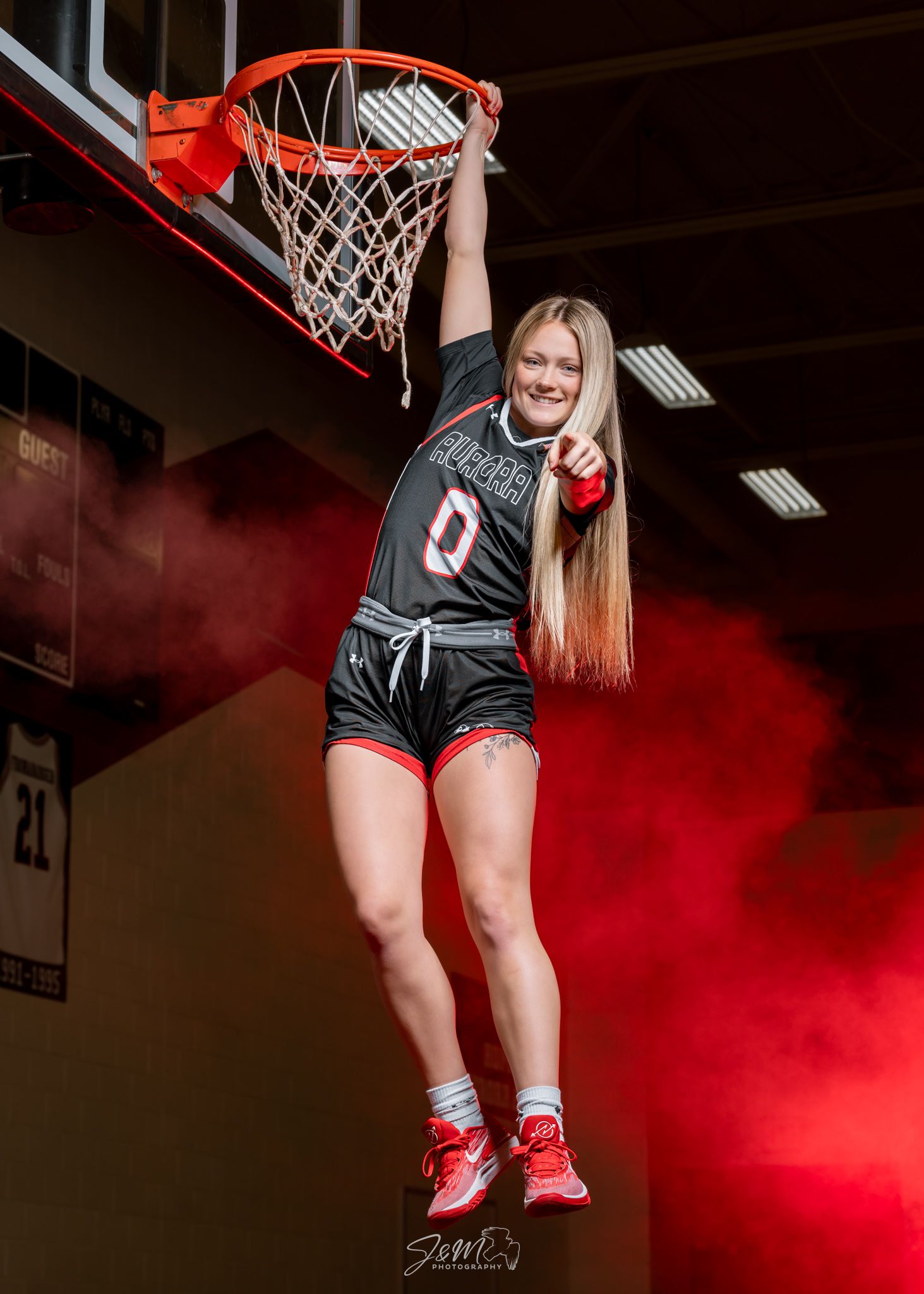 Basketball player jumps to hang on rim with red smoke effects in gymnasium.