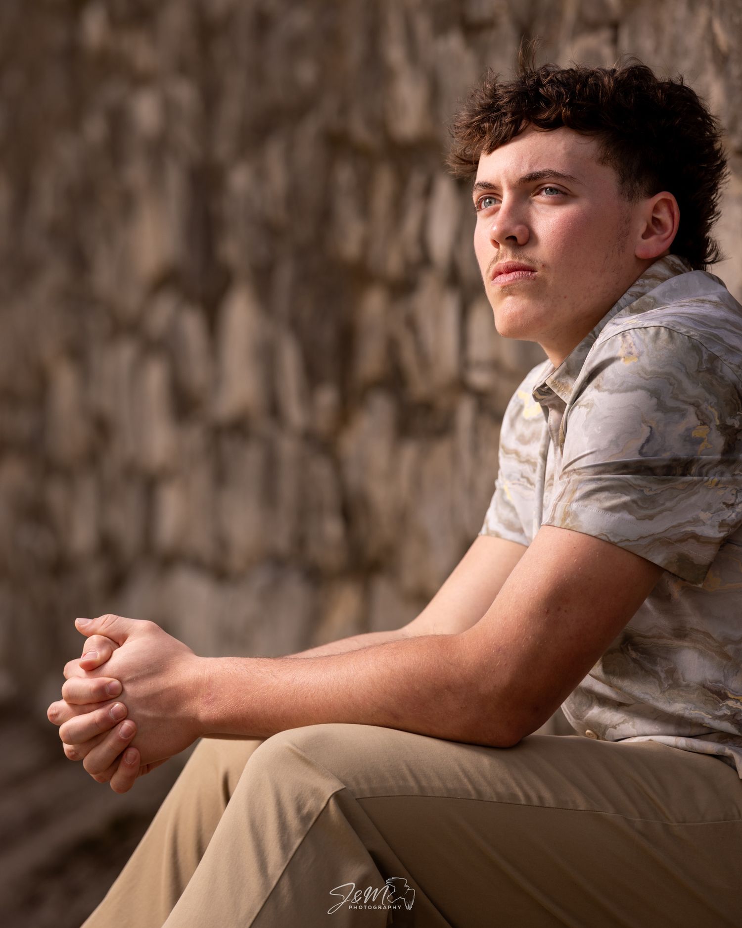 Portrait against stone wall showcasing casual style and natural lighting.