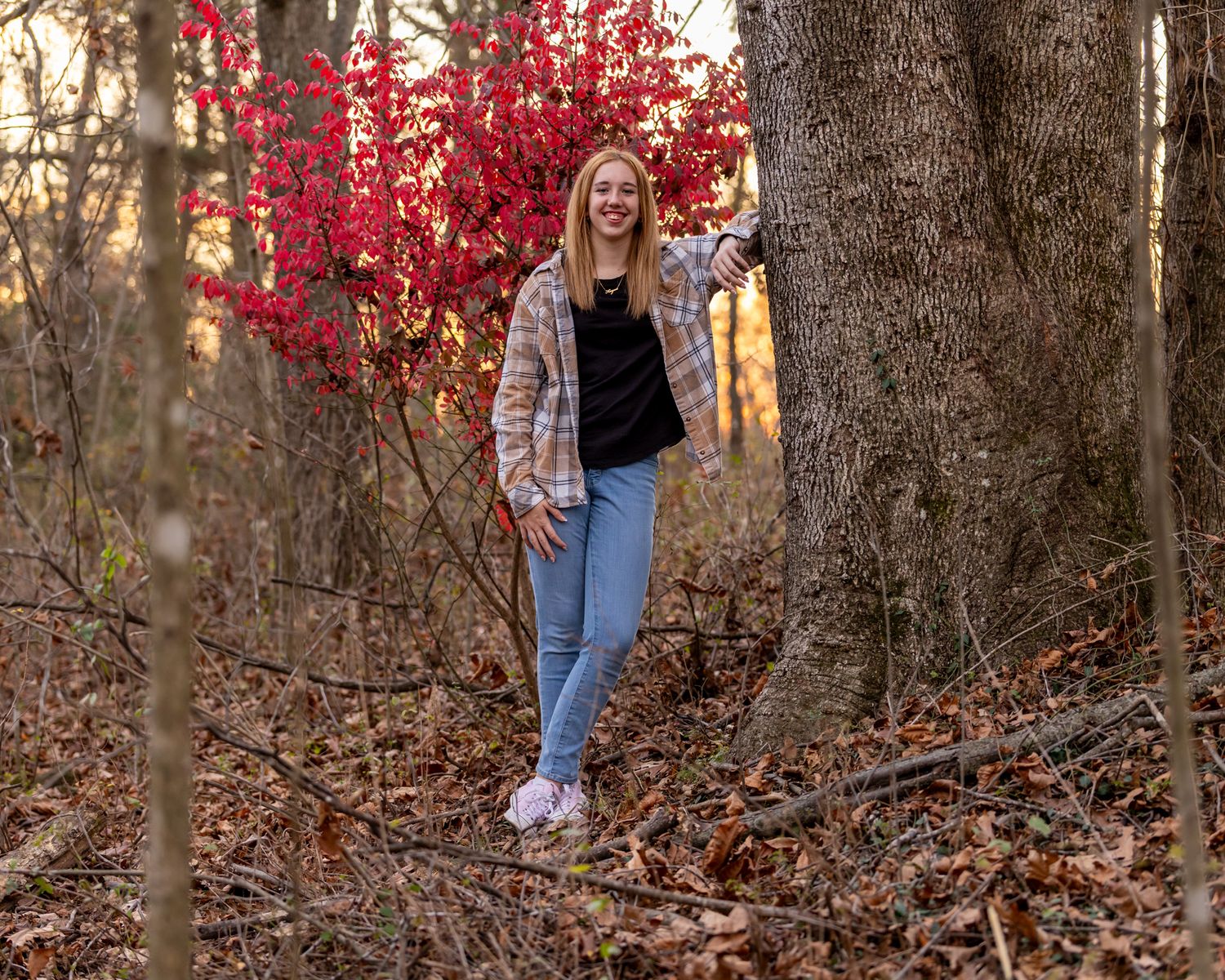 Athletic person stands in autumn forest with vibrant red foliage and fallen leaves.