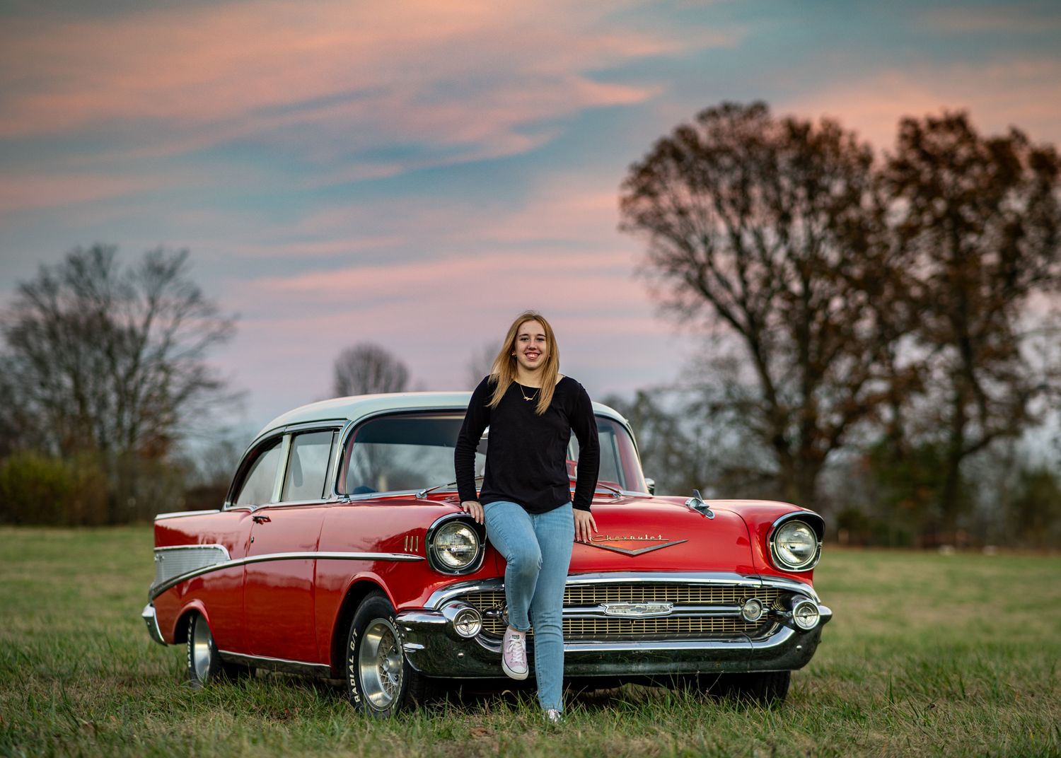 Person leaning against classic red Chevrolet during sunset in rural setting.