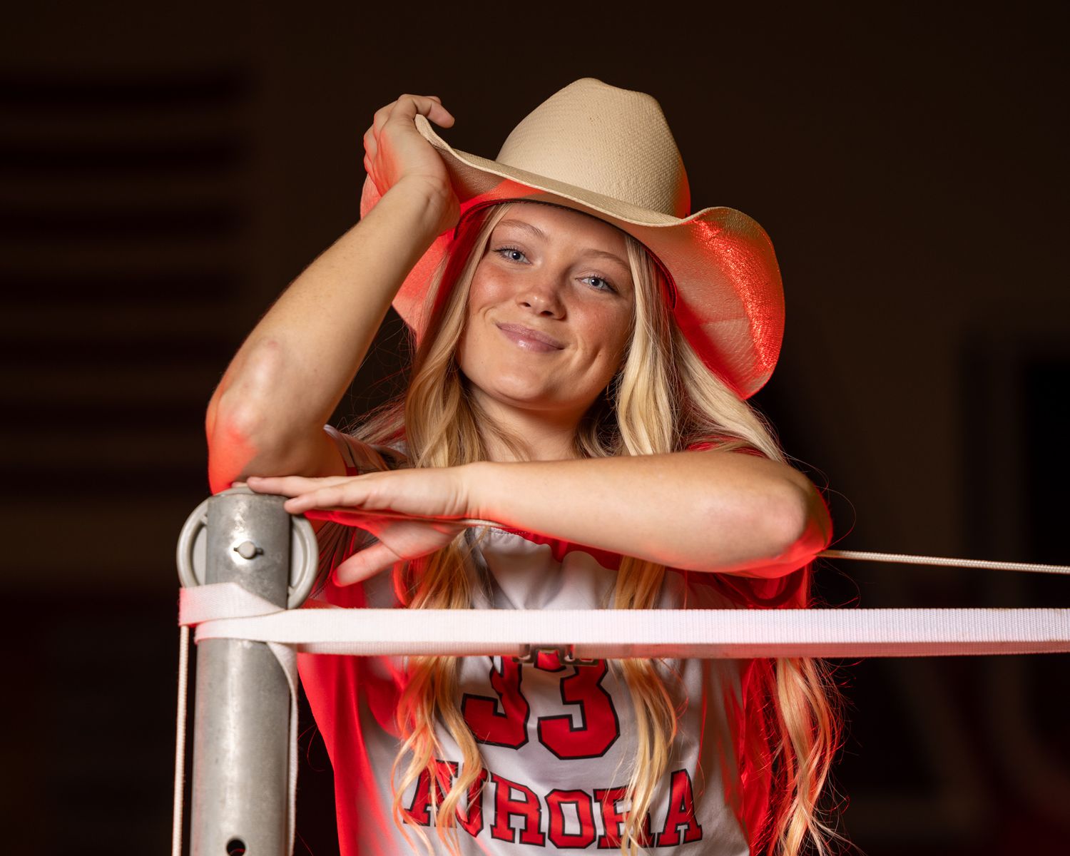 Athlete leans on railing wearing cowboy hat and sports jersey with dramatic lighting.